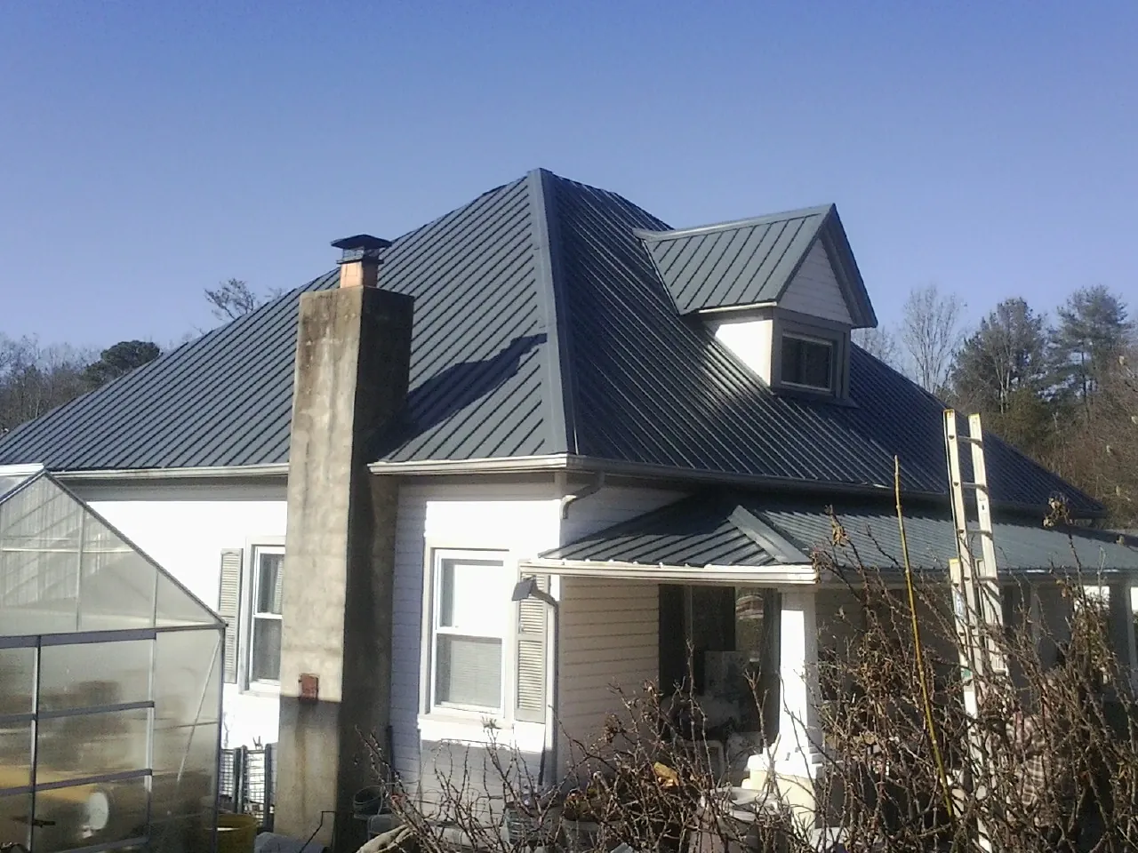 Dark blue standing seam metal roof on a white farmhouse with dormer — Slate & Tile Roof Repair by Roofing Brothers in Rome