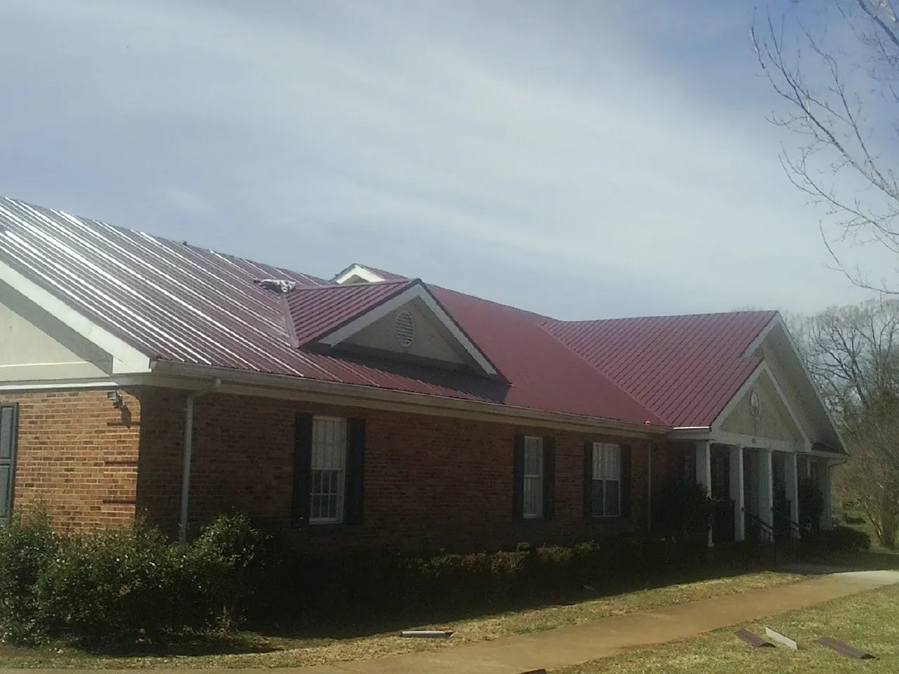 Red metal roof with gabled entries on a long brick building, from a Hail Damage Roof Repair job in Rome