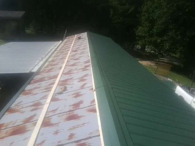 Old rusted panels beside newly installed green metal roofing — Wind Damage Roof Repair by Roofing Brothers in Rome