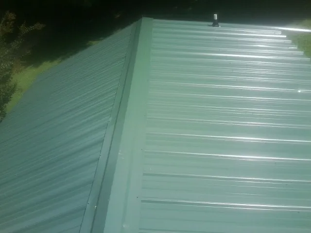 New green metal panels meeting at the ridge of a roof — Flat Roof Repair work by our crew in Rome